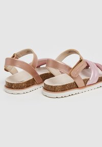 Roze en beige sandalen met een kurken zool, voorzien van kruisbanden en een gladde, glanzende bovenkant. Lichtgewicht ontwerp met een gestructureerde voetbed.