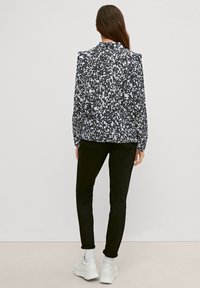 Zwart-wit gestreepte blouse met lange mouwen, in een getailleerd silhouet, gecombineerd met zwarte jeans en witte sneakers. Gladde stof met een subtiele glans.