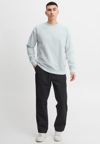 Lichtblauwe sweatshirt met ronde hals en lange mouwen, gecombineerd met zwarte, losse broek en witte sneakers. Eenvoudig, strak ontwerp.