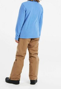 Jasnoniebieski polarowy top i brązowe wodoodporne spodnie, oba o luźnym kroju. Czarne buty z teksturowaną podeszwą i zamkami błyskawicznymi po bokach spodni.