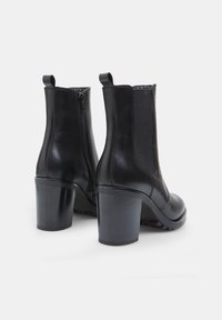 Botas de cuero negras hasta el tobillo con un diseño ajustado, tacón alto y grueso, cremallera lateral y paneles elásticos en ambos lados.