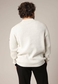 Crème kleurige ribgebreide trui met een ronde halslijn, lange mouwen en een comfortabele pasvorm. Subtiele textuur zonder zichtbare patronen of accenten.