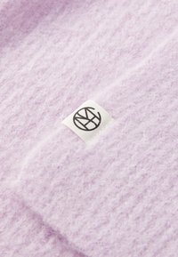 Soft lavender knit fabric with a small white rectangular label featuring a circular black logo stitched onto the material.
