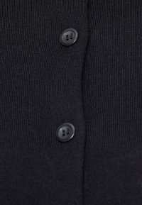 Σκούρο γκρι ύφασμα πλεκτού με ραβδωτή υφή, που διαθέτει δύο μαύρα κουμπιά στο μπροστινό μέρος, κοντινή λήψη της λωρίδας κουμπιών.