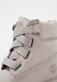 Gray suede ankle boot with textured gray laces, round eyelets, and logo. Features a padded collar and subtle stitching details.