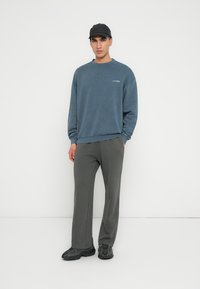 Hanorac din fleece albastru cu guler rotund, pantaloni de trening gri și o șapcă neagră, purtate cu adidași negri. Branding subtil pe hanorac.