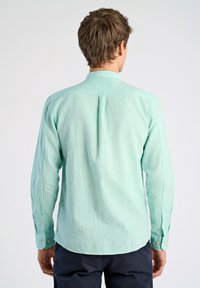 Camicia verde chiaro a maniche lunghe con tessuto testurizzato, polsini con bottone e un colletto piccolo. Presenta una piega sul retro per una maggiore libertà di movimento.