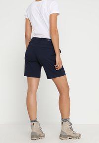 Marinblå shorts med skräddarsydd passform och elastiskt midjeband, tillverkade av lättviktigt tyg. Kombinerat med beige vandringsskor och grå strukturerade strumpor.