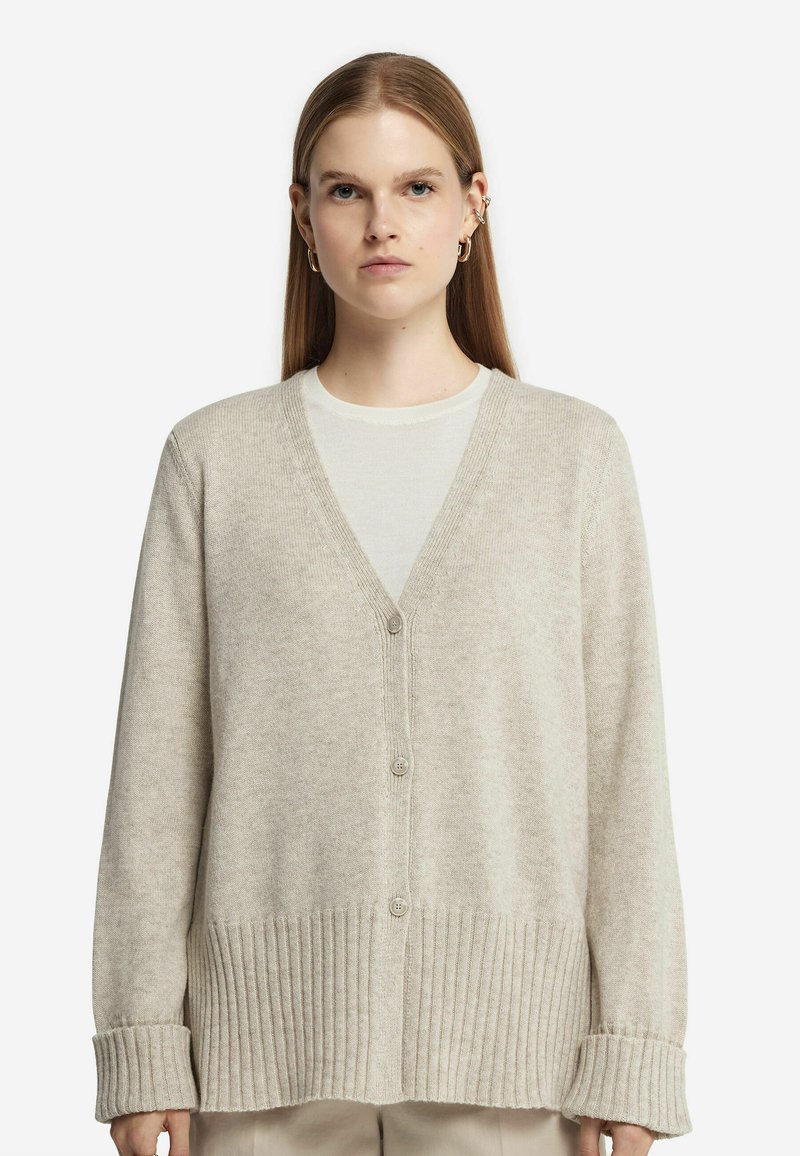 Beige cardigan med V-ringning, med knappstängning och ribbad nederdel. Tillverkad av mjukt stickat material med långa ärmar och avslappnad passform.