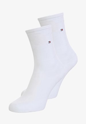 White cotton ankle socks with a ribbed cuff, featuring a small logo patch in red, white, and blue on the outer side.