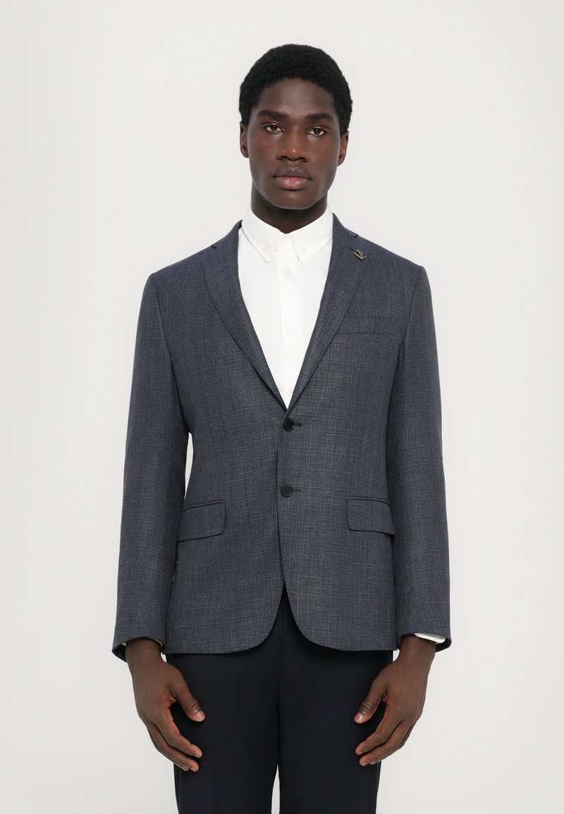 Marineblau strukturierter Blazer mit Revers, zwei vorderen Taschen und einem Knopfverschluss, getragen über einem weißen Hemd.
