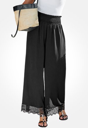 Pantalon noir à jambes larges avec une taille smockée et un bord en dentelle à l'ourlet, associé à un sac en paille beige avec un accent en cuir noir.