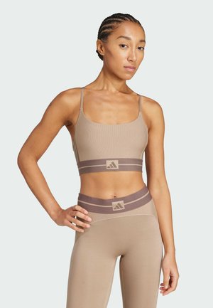 Beige geribbelde sportbeha met dunne bandjes en een contrasterende bruine logo-band. Bijpassende high-waisted leggings met een vergelijkbaar ontwerp en kleurenschema.