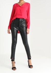 Blusa fucsia a maniche lunghe con scollatura a V, abbinata a pantaloni neri in ecopelle a vita alta con tasche con zip e spacchi alla caviglia.