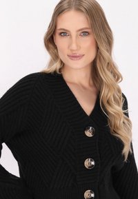 Schwarze Strickjacke mit V-Ausschnitt, diagonaler Rippstruktur und vier großen, runden Knöpfen mit subtiler Glanz.