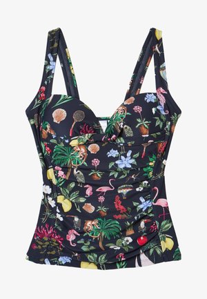 Femme debout pieds nus, portant un maillot de bain une pièce noir avec des motifs floraux et d’oiseaux colorés sur un fond beige uni.