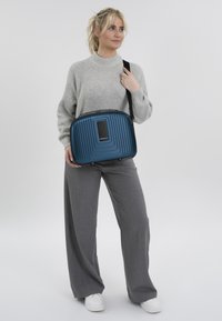 Blauwe harde schoudertas met horizontale ribbels, voorzien van een rechthoekig voorvak en een afneembare schouderband. Glad oppervlak en lichtgewicht ontwerp.