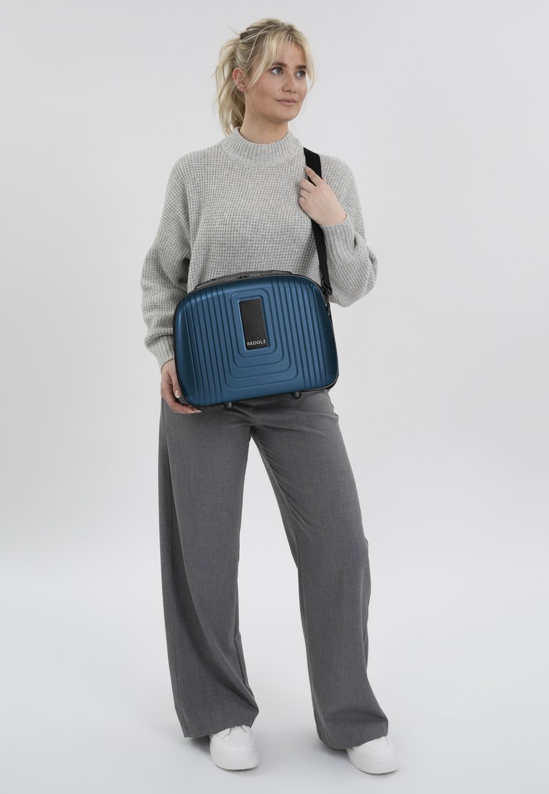 Blauwe harde schoudertas met horizontale ribbels, voorzien van een rechthoekig voorvak en een afneembare schouderband. Glad oppervlak en lichtgewicht ontwerp.