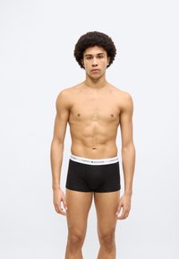 Μαύρα αντρικά εσώρουχα boxer με λευκή μέση που φέρει το κείμενο "TOMMY HILFIGER". Λείο ύφασμα, εφαρμοστό σχέδιο και μήκος έως τη μέση των μηρών.