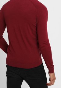 Suéter de punto en burdeos profundo, confeccionado con una suave tela de punto. Diseño ajustado con puños y dobladillo acanalados, presenta manguitos raglán.