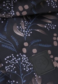 Czarna tkanina z kwiatowym wzorem w odcieniach niebieskiego i beżowego, z teksturowanym wzorem w jodełkę oraz czarną łatką z logo.