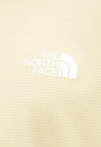 Μπεζ υφασμάτινη υφή με λευκό λογότυπο "THE NORTH FACE" και χαρακτηριστικό σχέδιο ημικυκλίου τυπωμένο στην επιφάνεια.