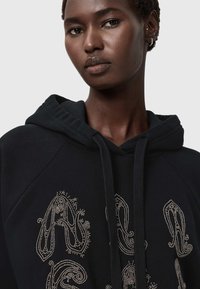 Czarna bluza z kapturem ze ściągaczem, ozdobiona metalowymi koralikami ułożonymi w wzór paisley na przodzie. Miękka w dotyku i o luźnym kroju.