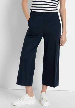 Navy wijdvallende culottes van zachte stof met een elastische tailleband en zijzakken, gecombineerd met witte sneakers.