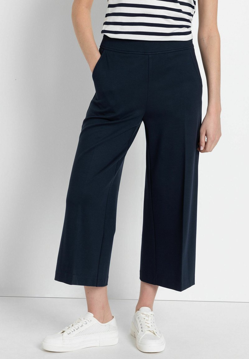 Navy wijdvallende culottes van zachte stof met een elastische tailleband en zijzakken, gecombineerd met witte sneakers.
