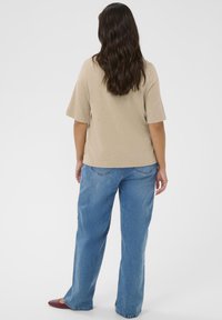 Beige top med korte ærmer og løs pasform, kombineret med lyseblå vidde-bukser. Stoffet virker glat med en subtil tekstur.