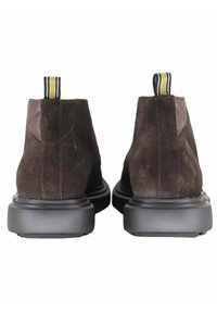 Stivaletti alla caviglia in pelle scamosciata marrone con suola in gomma nera, dotati di una linguetta di tiraggio a righe gialle e nere e dettagli in pelle marrone sul retro.