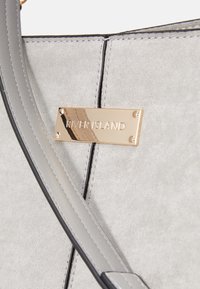 Szara torebka z sztucznego zamszu z złotą metalową plakietką z napisem "RIVER ISLAND." Posiada czarne wykończenia oraz gładką teksturę z dyskretnym przeszyciem.