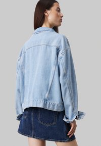 Lichtblauwe denimjack met verlaagde schouders en omgeslagen mouwen, gecombineerd met een donkerblauwe denimrok. Heeft een klassieke snit en een casual ontwerp.