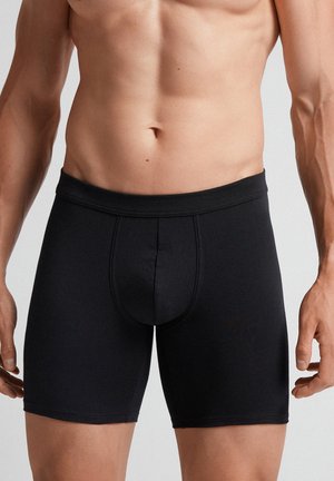 Boxer briefs negros con tejido elástico, un compartimento de soporte y una cinturilla suave. El diseño es ajustado y tiene una longitud a medio muslo.