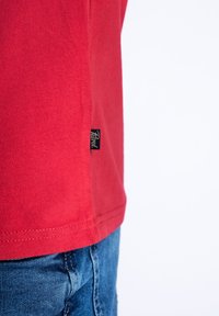 Red cotton t-shirt with a smooth texture, featuring a small black brand tag at the hem and a classic crew neckline design.