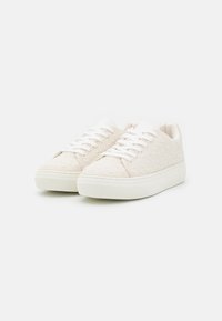 Beige sneakers with textured, dotted fabric, white laces, and a chunky white sole, featuring a smooth finish and minimalistic design.