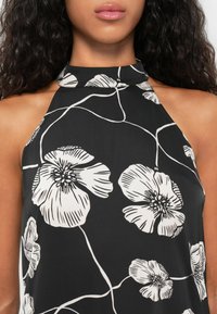 Vestido preto com decote halter, decorado com grandes padrões florais brancos e detalhes intrincados em linhas sobre um tecido suave.