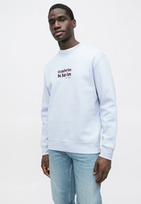 Világoskék pulóver kerek nyakkivágással és bordázott mandzsettákkal, elöl bordó "calvin klein" logó felirattal. Hétköznapi fazon.