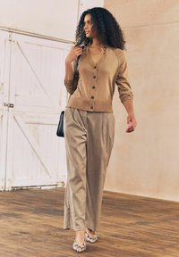 Lysebrun cardigan med knapper, parret med beige ternede bukser og sko med slangeskindsprint. Glat stof og afslappet pasform.