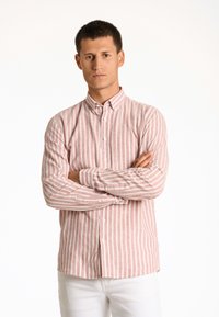 Camicia a righe con bottoni in rosa chiaro e bianco, realizzata in tessuto traspirante, con maniche lunghe e colletto classico. Indossata con pantaloni bianchi.