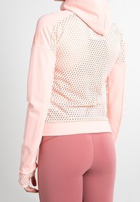 Light pink hooded jacket with perforated back panel and matching light pink leggings worn by a person shown from the back.