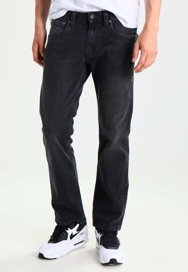 Jeans de mezclilla negra con un corte recto, cinco bolsillos y cierre de botón. Llevados con zapatillas negras y blancas. Textura suave.