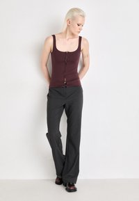 Top aderente bordeaux con dettagli di bottoni frontali, abbinato a pantaloni a gamba larga grigio scuro e stivaletti neri con accenti bordeaux.