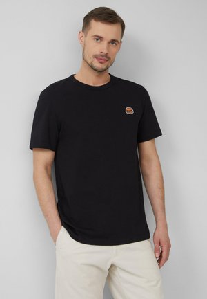 Schwarzes Baumwoll-T-Shirt mit kurzen Ärmeln und Rundhalsausschnitt, mit einem kleinen, gestickten Hamburger-Graphic auf der linken Brust.