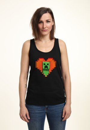 Top nero senza maniche con una grafica pixelata di un creeper verde all'interno di un design a cuore arancione. Realizzato in tessuto morbido con una forma aderente.