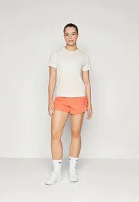 Heled beez T-särk ja korallvärvi lühikesed püksid, mis on valmistatud hingavast kangast. Valged sportlikud kingad ja sokid. Lihtne disain logode aktsentidega.