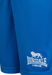 Mėlynos sportinės šortai, pagaminti iš lygaus audinio. Pavyzdžiuoja baltą išsiuvinėtą logotipą su liūtu ir prekės ženklu apatinėje dalyje.