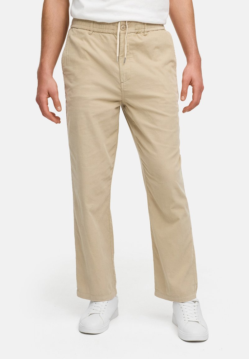 Pantalones de algodón beiges con cintura elástica y cordón, con un corte relajado y bolsillos laterales, combinados con zapatillas blancas.