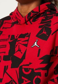 Puna huppari mustilla graafisilla kuvioilla ja valkoisella Jordan-logolla. Ominaisuuksiin kuuluu pehmeä tekstuuri ja rento istuvuus.