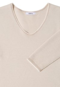 Pull beige à manches longues en maille avec décolleté en V et bordure blanche sur le col et les poignets, étiquette "CECIL" à l'intérieur du col.